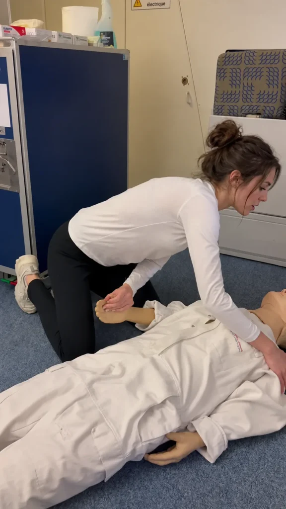 A trainee practises a first-aid assessment with a mannequin in a cabin training environment.